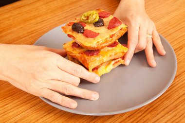 Caucasian white person holding delicious pizza slices in grey plate on brown wooden table clipart