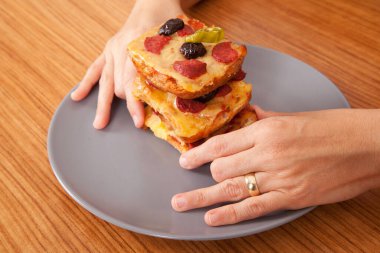 Caucasian white person holding delicious pizza slices in grey plate on brown wooden table clipart