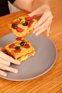 Caucasian white person holding delicious pizza slices in grey plate on brown wooden table clipart