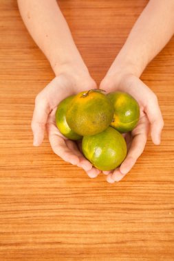 Genç beyaz erkek elinde taze sarı ve yeşil mandalinalar, kahverengi ahşap masanın üzerinde.