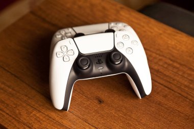 Sony PS5 Wireless Controller, meşe ağacından bir masa üzerinde, PlayStation beş oyun konsolundan oluşan bir video oyun markasıdır. Çekim tarihi İstanbul Türkiye 01 Mayıs 2025