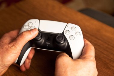 Sony PS5 Wireless Controller, meşe ağacından bir masa üzerinde, PlayStation beş oyun konsolundan oluşan bir video oyun markasıdır. Çekim tarihi İstanbul Türkiye 01 Mayıs 2025