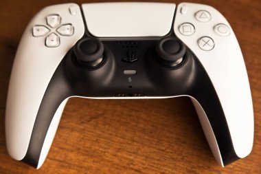 Sony PS5 Wireless Controller, meşe ağacından bir masa üzerinde, PlayStation beş oyun konsolundan oluşan bir video oyun markasıdır. Çekim tarihi İstanbul Türkiye 01 Mayıs 2025
