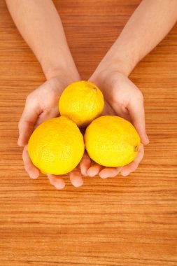 Kahverengi ahşap masanın üzerinde taze sarı limon tutan beyaz bir erkek.