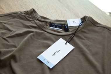 Koyu yeşil Lefties XL yeni tişört ve boş etiket, ahşap zeminde, 29 Mart 2025 İstanbul Maltepe Türkiye Maltepe Solakları mağazası