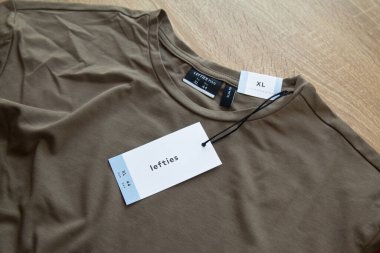 Koyu yeşil Lefties XL yeni tişört ve boş etiket, ahşap zeminde, 29 Mart 2025 İstanbul Maltepe Türkiye Maltepe Solakları mağazası