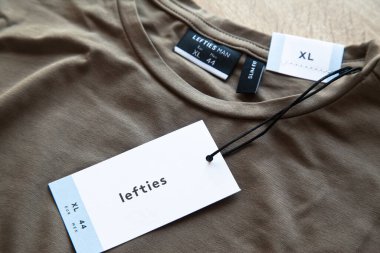 Koyu yeşil Lefties XL yeni tişört ve boş etiket, ahşap zeminde, 29 Mart 2025 İstanbul Maltepe Türkiye Maltepe Solakları mağazası