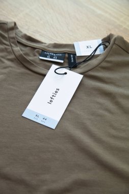 Koyu yeşil Lefties XL yeni tişört ve boş etiket, ahşap zeminde, 29 Mart 2025 İstanbul Maltepe Türkiye Maltepe Solakları mağazası