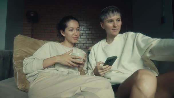 两个年轻女人坐在家里沙发上 拿着手机 慢吞吞地走着 — 图库视频影像