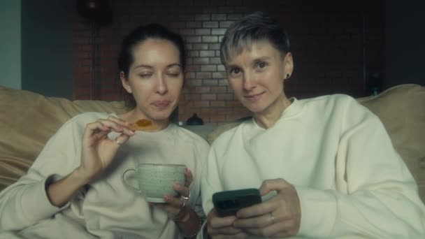 二人の若い女性は自宅で一緒にリラックスしながら 彼らのスマートフォンで面白いビデオを見て スローモーション — ストック動画