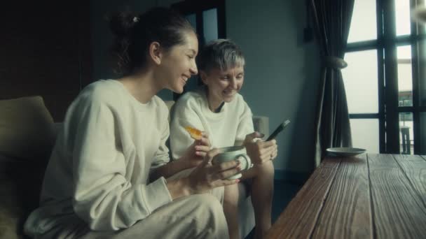 Две Молодые Женщины Смотрят Смешные Видео Смартфоне Расслабляясь Вместе Дома — стоковое видео