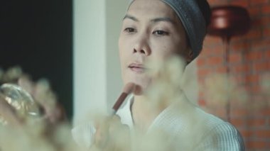 Young asian transgender queer man does his makeup in his room while getting ready for a date