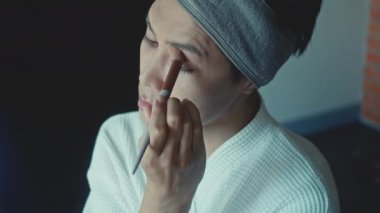 Young asian transgender queer man does his makeup in his room while getting ready for a date