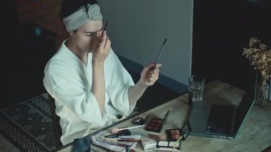Young Asian transgender queer man learns how to do makeup online on laptop