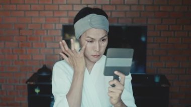Young asian transgender queer man does his makeup in his room while getting ready for a date
