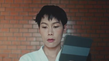 Young asian transgender queer man does his makeup in his room while getting ready for a date