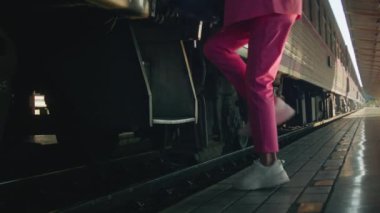A young woman in a pink suit boards a train in slow motion, close-up shot