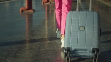 A young woman in a pink suit and with a suitcase walking on the platform near the train in slow motion, close-up follow shot