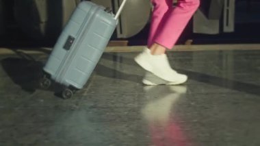 A young woman in a pink suit and with a suitcase walking on the platform near the train in slow motion, close-up follow shot