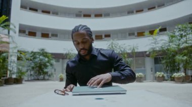 Sokakta dizüstü bilgisayarla çalışan genç bir Afro-Amerikalı iş adamı. Yakışıklı iş adamı portresi, yavaş çekim bmpcc 6k çekim