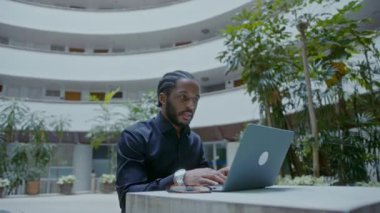Sokakta dizüstü bilgisayarla çalışan genç bir Afro-Amerikalı iş adamı. Yakışıklı iş adamı portresi, yavaş çekim bmpcc 6k çekim