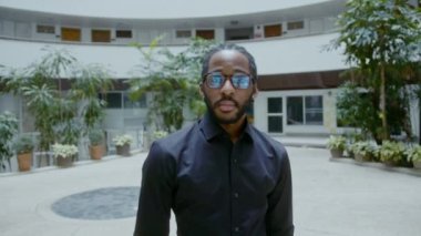Genç Afro-Amerikan iş adamı şirket binasının önünde duruyor. Yakışıklı iş adamı portresi, yavaş çekim bmpcc 6k çekim