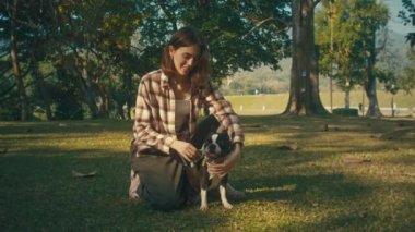 Young woman plays with her Boston Terrier at sunset in park in slow motion