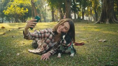 Young woman takes selfie with her Boston Terrier at sunset in park in slow motion