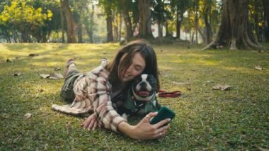 Young woman takes selfie with her Boston Terrier at sunset in park in slow motion