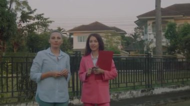 Elinde belgelerle pembe takım elbiseli genç bir emlakçı potansiyel bir müşteriye ev gösteriyor. Yavaş çekim 6k çekim