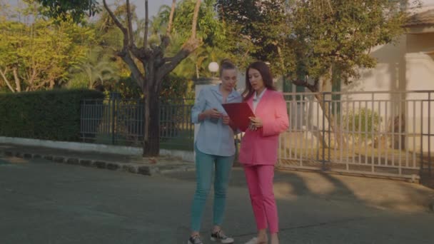 一名身穿粉色西装的年轻女性房地产经纪人手头上拿文件 向一位潜在客户展示房屋 慢动作6K弹 — 图库视频影像