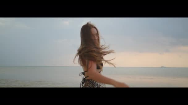 美しい長髪の少女はゆっくりとした動きで日没のビーチで渦巻く 変成岩ショット — ストック動画