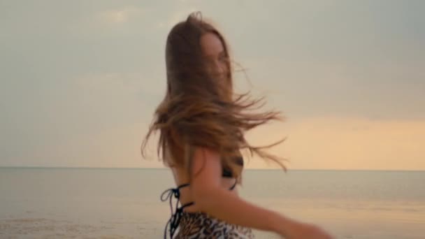 美しい長髪の少女はゆっくりとした動きで日没のビーチで渦巻く 変成岩ショット — ストック動画