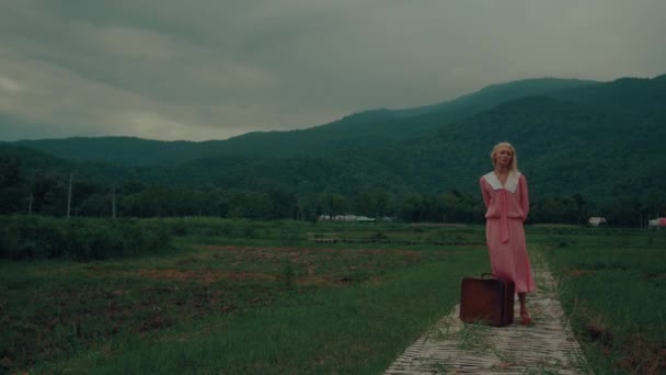 穿着复古服装 提着一个复古手提箱的小女孩站在一座山前 高质量的4K慢镜头 — 图库视频影像