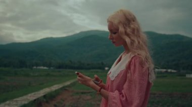 Klasik elbiseli genç kız telefonunu bir dağın önünde kullanıyor. Yüksek kalite 4 bin yavaş çekim görüntüsü
