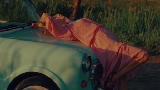Blondynka Różowej Sukience Leży Masce Turkusowego Samochodu Retro Zachodzie Słońca — Wideo stockowe