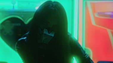 Işıkların arasında kameraya bakan siber punk maskeli bir Asyalı kadın. Ağır çekim. Yüksek kalite 4K görüntü.