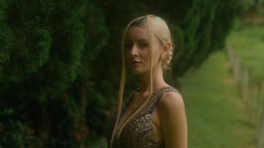 Çekici kadın selvi ağaçlarının olduğu bir orman manzarasına karşı poz veriyor. Selvi ağaçlarının yanında durup kameraya bakan zarif kız. Ormanda manken olmak. Kara büyü 6k görüntüsü