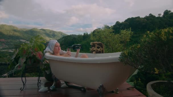 一个女人带着一瓶葡萄酒和美丽的山景正在洗澡 黑魔法6K镜头 — 图库视频影像