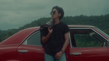 Kahverengi deri ceketli vahşi bir erkek fatma kız klasik kırmızı arabasına yaslanıyor. Kara büyü 6k görüntüsü