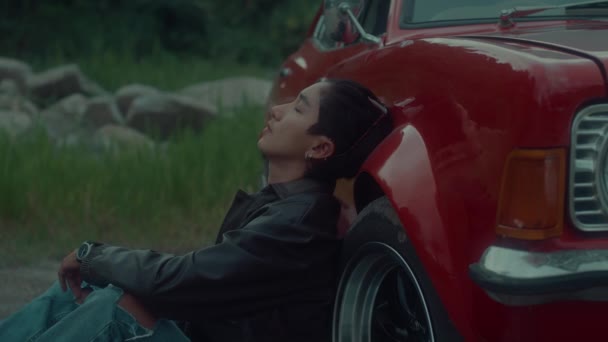 一个穿着棕色皮夹克的残忍女孩悲伤地坐在她那辆经典的红色轿车旁边 黑魔法6K镜头 — 图库视频影像