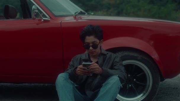一个穿着棕色皮夹克的残忍女孩坐在她经典的红色轿车外面 用手机发短信 黑魔法6K镜头 — 图库视频影像