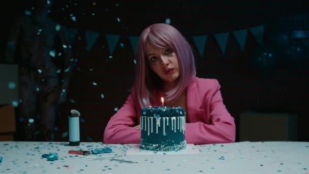 悲伤的粉红头发的生日女孩 穿着粉红夹克坐在桌子旁 带着蓝色的生日蛋糕 在一间昏暗的房间里把蜡烛吹灭 还带着生日蛋糕 — 图库视频影像
