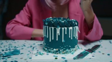 Üzücü pembe saçlı, makyajlı, pembe ceketli bir doğum günü kızı masaya oturmuş, büyük bir mavi doğum günü pastası alıyor ve elleri ile karanlık bir odada doğum günü süslemeleri ile yiyor. Yüksek