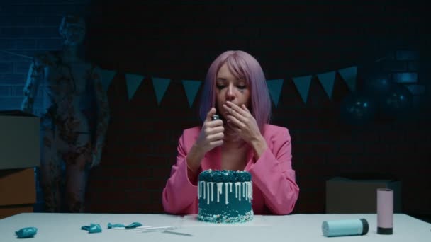 悲伤的粉红头发的生日女孩穿着粉红夹克坐在桌旁 带着蓝色的生日蛋糕 在一间装饰着生日装饰品的黑暗的房间里点燃了一支蜡烛 高质量的4K镜头 — 图库视频影像