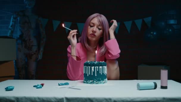 穿着粉红西装的悲哀的粉红头发的生日女孩坐在桌子旁 带着蓝色的生日蛋糕 在一间装饰着生日装饰品的黑暗的房间里吹灭了蜡烛 高质量4K — 图库视频影像