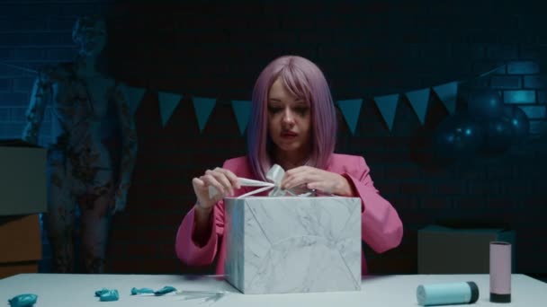 身穿粉红西装的悲伤的粉红头发的生日女孩坐在桌旁 在一间装饰着生日装饰品的黑暗的房间里打开礼物 高质量的4K镜头 — 图库视频影像
