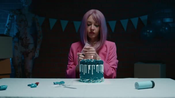 身穿粉红夹克的粉红发女寿星坐在桌子旁 带着蓝色的生日蛋糕 在一间装饰有生日装饰的黑暗房间里 发射了一个彩蛋炮 高质量的 — 图库视频影像