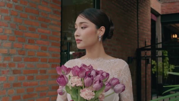 チューリップの結婚式の花束 結婚式のための花嫁の自然な構造を保持する通りにポーズするレースのウェディングドレッシングで魅力的な若いタイの花嫁の肖像画 高品質の4K映像 — ストック動画