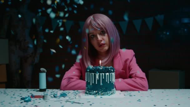 悲伤的粉红头发的生日女孩 穿着粉红夹克坐在桌子旁 带着蓝色的生日蛋糕 在一间昏暗的房间里把蜡烛吹灭 还带着生日蛋糕 — 图库视频影像